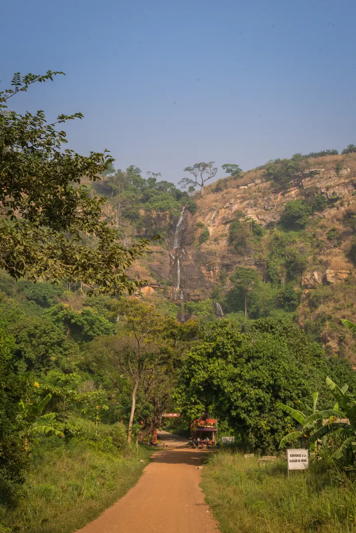 La cascade de Kpimé vue depuis la vallée : un mince filet d’eau dévale la paroi rocheuse au milieu de la forêt tropicale, au nord de Kpalimé