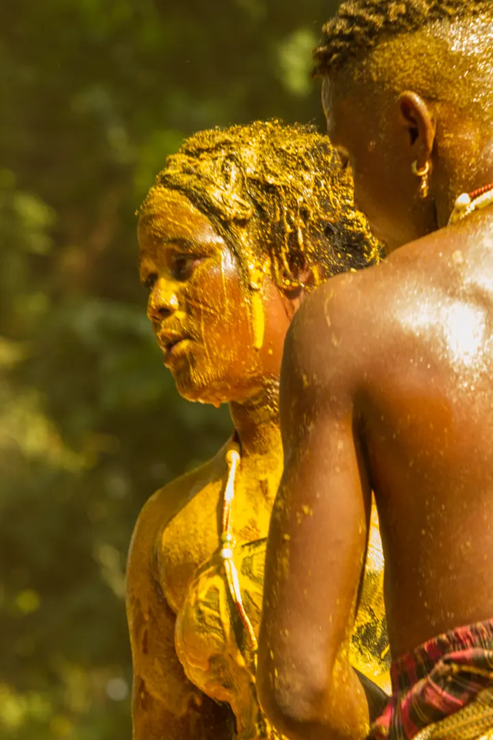 Portrait de profil d’un participant aux Vodun Days, le visage et les épaules recouverts de poudre ocre, le regard tourné vers la cérémonie