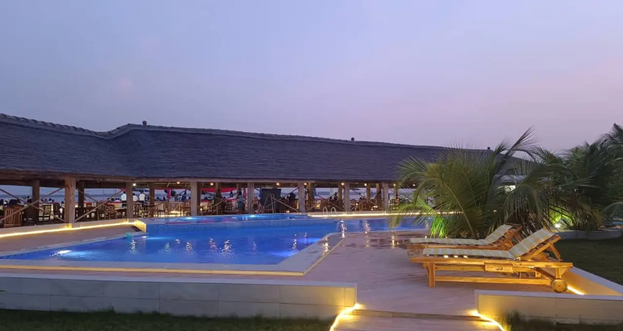 Piscine et paillote d’un hébergement au crépuscule, transats alignés le long du bassin éclairé