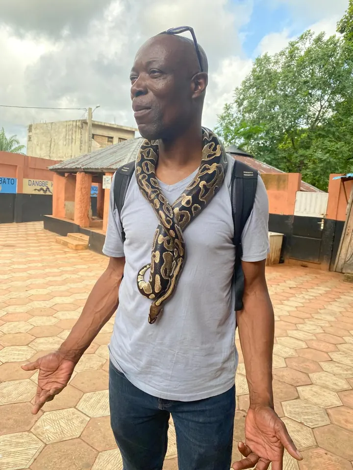 Tony, fondateur et guide de NESS Voyage, un python royal enroulé autour du cou dans la cour du temple des Pythons à Ouidah